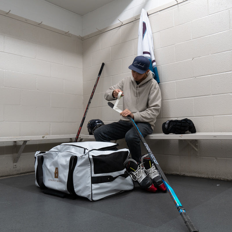 Person sitting on a bench with hockey equipment in a locker room.